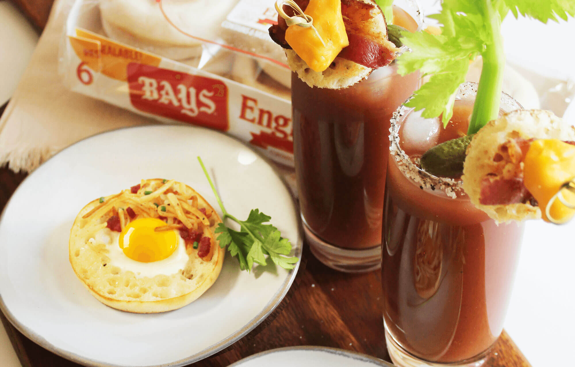 BAYS WITH EGGS AND BACON NEXT TO A RED DRINK WITH CELERY CHEESE AND BACON AS A GARNISH